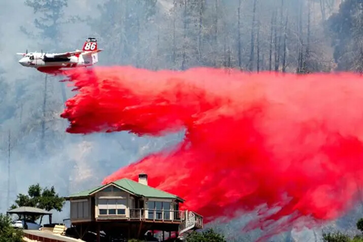 Un avión cisterna arroja retardante detrás de una casa mientras lucha contra un incendio cerca de Calistoga, California, el 2 de julio de 2024. (Noah Berger/AP Photo)