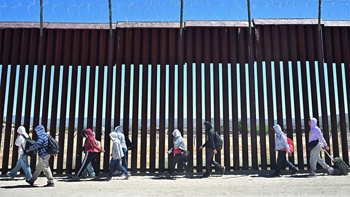 Migrantes caminan por el lado estadounidense del muro fronterizo en Jacumba Hot Springs, California, tras cruzar desde México, el 5 de junio de 2024. (Frederic J. Brown/AFP)