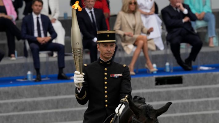 El coronel Thibault Vallette, del Cadre Noir de Saumur, el Instituto Francés del Caballo y la Equitación, porta la antorcha olímpica durante el desfile del Día de la Bastilla el domingo 14 de julio de 2024 en París. (AP Photo/Louise Delmotte)