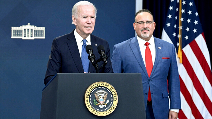 El secretario de Educación, Miguel Cardona (dcha.), observa al presidente Joe Biden mientras pronuncia un discurso sobre la prueba beta del portal de alivio de la deuda estudiantil, en el Auditorio South Court del Edificio de Oficinas Ejecutivas Eisenhower, junto a la Casa Blanca, en Washington, el 17 de octubre de 2022. Brendan Smialowski/AFP vía Getty Images)
