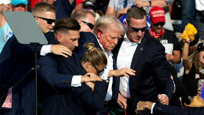 El expresidente Donald Trump con sangre en la cara rodeado de agentes del servicio secreto mientras es sacado del escenario en un acto de campaña en Butler, Pensilvania, el 13 de julio de 2024. (Rebecca Droke/AFP vía Getty Images)