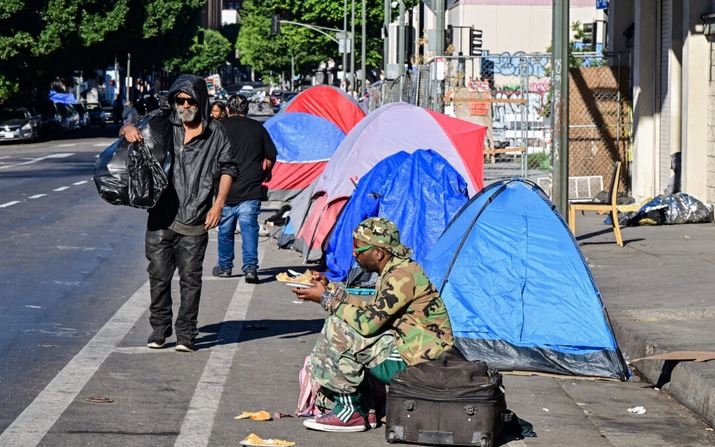 Un hombre sin hogar sentado sobre una maleta en una calle llena de tiendas de campaña en el centro de Los Ángeles el 22 de noviembre de 2023. (Frederic J. Brown/AFP vía Getty Images)