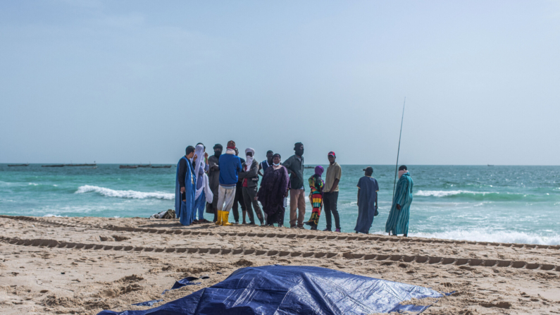 Personas presentes miran los cuerpos cubiertos de migrantes que perecieron en un naufragio frente a la costa de Mauritania, en una playa fuera de Nuakchot, el 24 de julio de 2024.  (MED EMINE RAJEL/AFP via Getty Images)