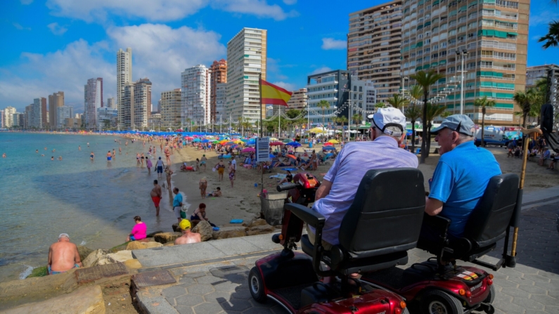 Ancianos en scooters de movilidad miran a la gente que disfruta de la Playa de Levante de Benidorm el 7 de junio de 2022. (Foto de JOSE JORDAN/AFP via Getty Images)