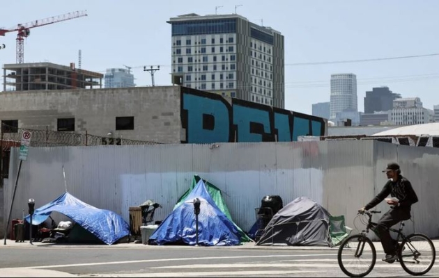 Un ciclista pasa por delante de un campamento de personas sin hogar en la comunidad de Skid Row, en Los Ángeles, el 28 de junio de 2024. (Mario Tama/Getty Images)