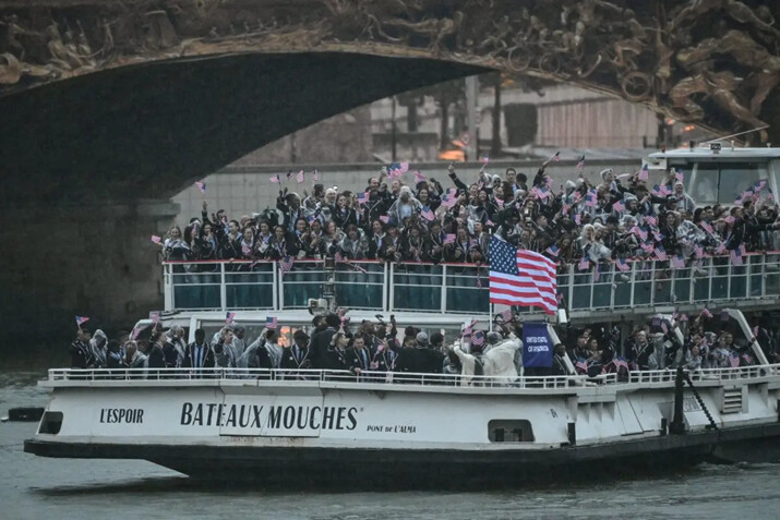 Los atletas de la delegación estadounidense ondean banderas mientras navegan en un bote por el río Sena durante la ceremonia de apertura de los Juegos Olímpicos de París 2024, en París, el 26 de julio de 2024. (Miguel Medina/AFP vía Getty Images)