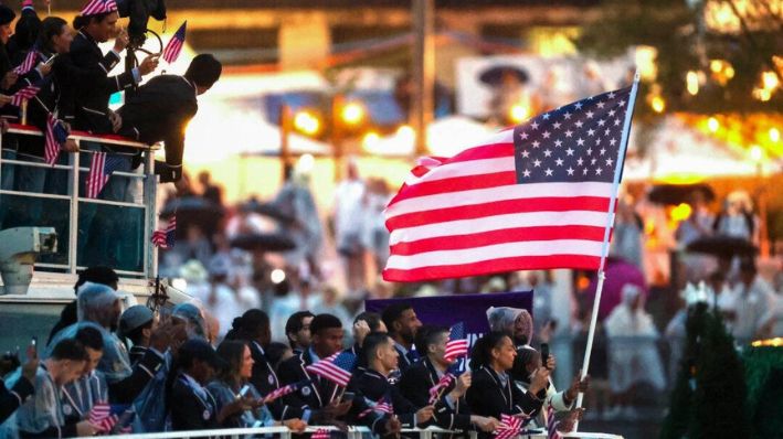 Lebron James, abanderado del equipo de Estados Unidos, es visto ondeando su bandera en un bote con sus compañeros de equipo a lo largo del río Sena durante la ceremonia de apertura de los Juegos Olímpicos de París 2024 en París el 26 de julio de 2024. (Steph Chambers / POOL / AFP vía Getty Images)