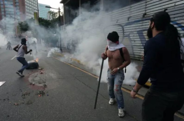 Manifestantes corren para ponerse al cubierto de los gases lacrimógenos mientras partidarios de la oposición venezolana protestan en Caracas, Venezuela, el 29 de julio de 2024. (Alexandre Meneghini/Reuters)