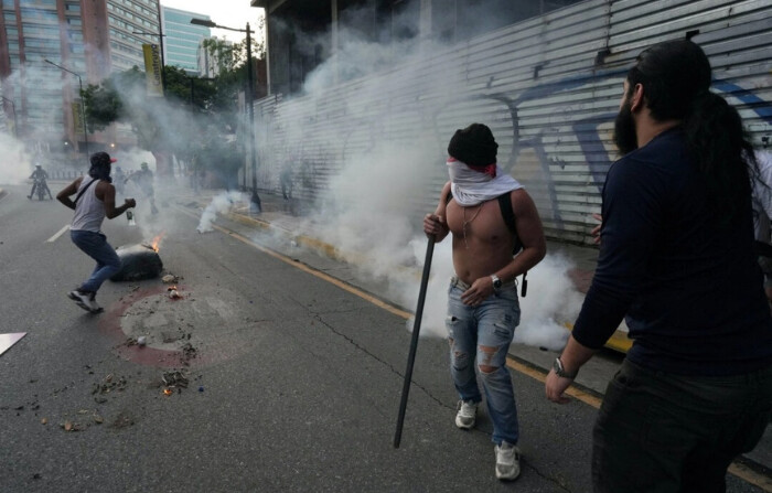 Manifestantes corren para ponerse a cubierto de los gases lacrimógenos mientras simpatizantes de la oposición venezolana protestan tras el anuncio del Consejo Nacional Electoral de que el presidente de Venezuela, Nicolás Maduro, había ganado las elecciones presidenciales, en Caracas, Venezuela, el 29 de julio de 2024. (Alexandre Meneghini / Reuters)
