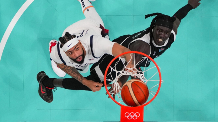 Anthony Davis (izq.), #14, de Estados Unidos, y Wenyen Gabriel (der.), #09, de Sudán del Sur, observan el balón en el partido de baloncesto masculino de la ronda preliminar del grupo C entre Estados Unidos y Sudán del Sur durante los Juegos Olímpicos de París 2024 en el estadio Pierre-Mauroy en Villeneuve-d'Ascq, norte de Francia, el 31 de julio de 2024. (AFP vía Getty Images)