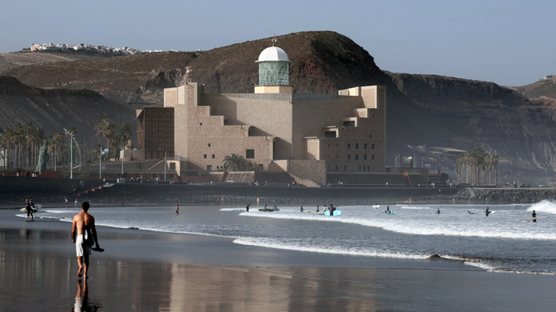 Varias personas pasean por una playa de la ciudad canaria de Las Palmas, con el auditorio Alfredo Kraus al fondo, el 28 de enero de 2024. (Foto de THOMAS COEX/AFP vía Getty Images)