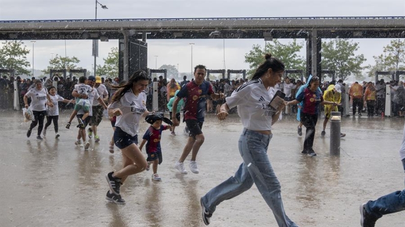 Aficionados corren bajo la lluvia previo al partido amistoso del clásico del fútbol español entre Real Madrid vs Barcelona, este sábado 3 de agosto de 2024, en el Metlife Stadium en New Jersey (EE.UU.). EFE/ Ángel Colmenares