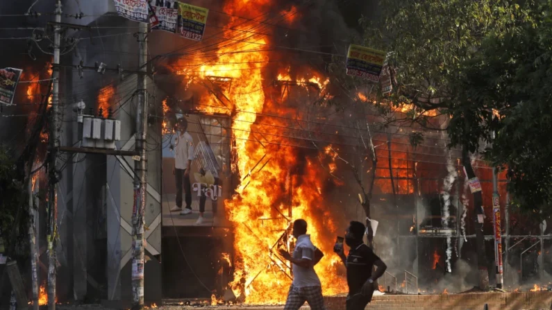 Unos hombres corren frente a un centro comercial que fue incendiado durante una manifestación contra la primera ministra Sheikh Hasina y su gobierno, en Dacca, Bangladesh, el domingo 4 de agosto de 2024. (Foto AP/Rajib Dhar)