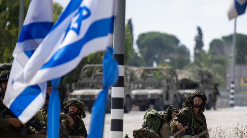 Soldados de las FDI vigilan cerca de una bandera israelí ondeante fuera del Kibbutz Kfar Aza, donde decenas de civiles fueron asesinados días antes en un ataque de militantes de Hamas cerca de la frontera con Gaza, el 10 de octubre de 2023 en Kfar Aza, Israel. (Alexi J. Rosenfeld/Getty Images)