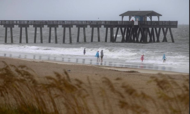 Los bañistas caminan cerca del muelle de Tybee mientras el viento y la lluvia de la tormenta tropical Debby comienzan a llegar a tierra en Tybee Island, Georgia, el 5 de agosto de 2024. (Stephen B. Morton/Foto AP)