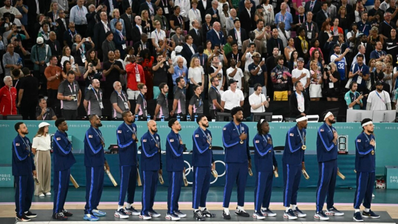 El equipo masculino de baloncesto de Estados Unidos celebra su victoria en los Juegos Olímpicos de París 2024 en el podio durante el himno nacional tras ganar la medalla de oro masculina de baloncesto contra Francia el 10 de agosto de 2024. (Paul Ellis/AFP)
