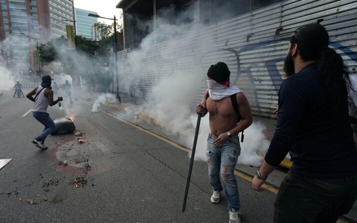 Manifestantes corren para protegerse de los gases lacrimógenos mientras partidarios de la oposición venezolana protestan tras el anuncio del Consejo Nacional Electoral de que el presidente de Venezuela, Nicolás Maduro, ganó las elecciones presidenciales, en Caracas, Venezuela, el 29 de julio de 2024. (Alexandre Meneghini/Reuters)