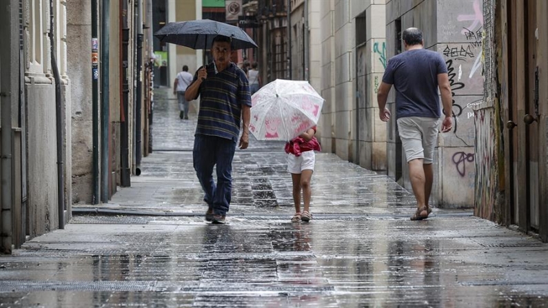 Varias personas caminan bajo la lluvia por una calle del centro de Valencia (España). EFE/Manuel Bruque