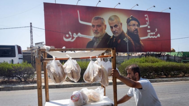 Un hombre empuja su carro de comida delante de una valla publicitaria en la que aparecen el fallecido líder de Hamás Ismail Haniyeh; el general Qasem Soleimani, que sirvió en la Guardia Revolucionaria iraní; y el alto comandante de Hezbolá Fuad Shukr, en Beirut, Líbano, el 6 de agosto de 2024. (Chris McGrath/Getty Images)