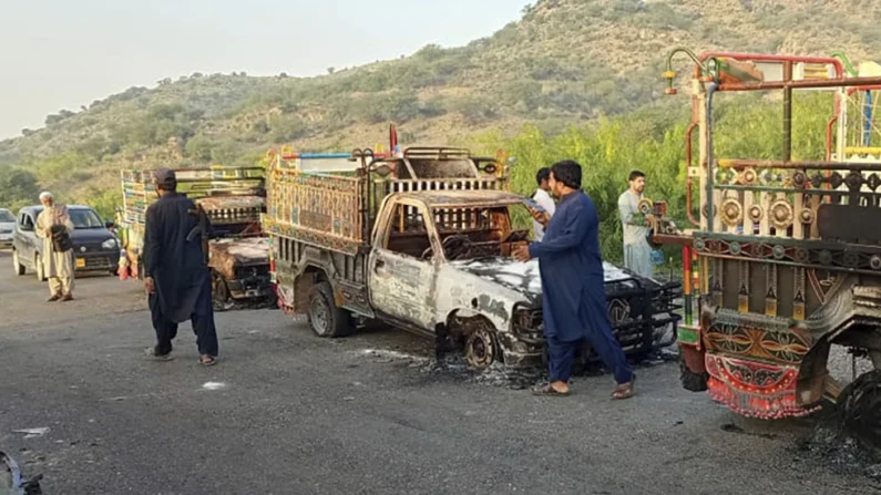 Varias personas observan vehículos incendiados por hombres armados después de que mataron a los pasajeros el lunes 26 de agosto de 2024, en una carretera de Musakhail, un distrito de la provincia de Baluchistán, en el suroeste de Pakistán.  (AP Foto/Rahmat Khan)