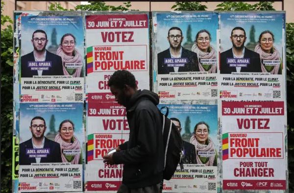 Un hombre pasa junto a los carteles electorales del candidato del Nouveau Front Populaire, Adel Amara, el 5 de julio de 2024. (Emmanuel Dunand/AFP)