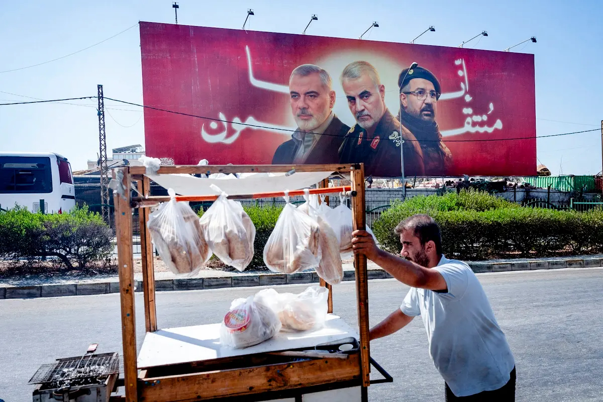 Un hombre empuja su carrito de comida delante de un cartel publicitario en el que aparecen el fallecido líder de Hamás Ismail Haniyeh; el general Qasem Soleimani, que sirvió en la Guardia Revolucionaria iraní; y el alto comandante de Hezbolá Fuad Shukr, en Beirut, Líbano, el 6 de agosto de 2024. (Chris McGrath/Getty Images)