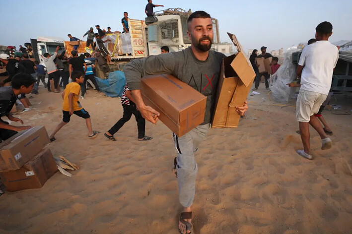 Palestinos transportan cajas de ayuda humanitaria tras sacar camiones del muelle Trident, construido por Estados Unidos, cerca de Nuseirat, en el centro de la Franja de Gaza, el 18 de mayo de 2024. (AFP vía Getty Images)