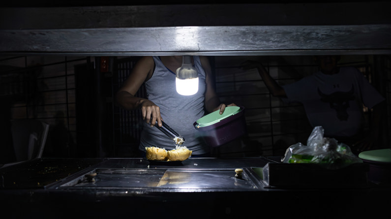 Una persona vende comida ayudado con un bombillo en medio de la oscuridad durante un corte eléctrico, el 29 de febrero de 2024 en Maracaibo, Venezuela. (EFE/ Henry Chirinos)