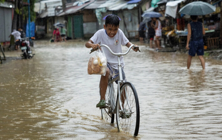 Un niño que lleva una bolsa de plástico con pan y huevos, anda en bicicleta por una carretera inundada tras las fuertes lluvias provocadas por la tormenta tropical Yagi, conocida localmente como Enteng, en Baras, provincia de Rizal, Filipinas, el 2 de septiembre de 2024. (Eloisa Lopez/Reuters)