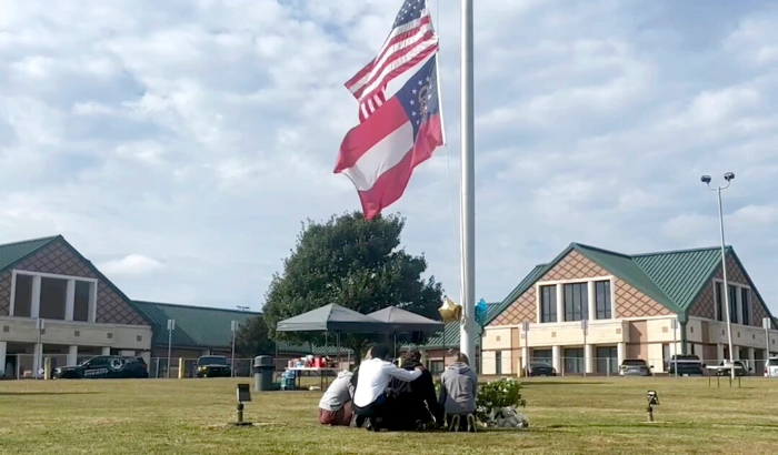 La gente se reúne en el asta de la bandera fuera de la entrada de la Escuela Secundaria Apalachee en Winder, Georgia, el 5 de septiembre de 2024, un día después de los tiroteos mortales en la escuela. (Sharon Johnson/Foto AP)