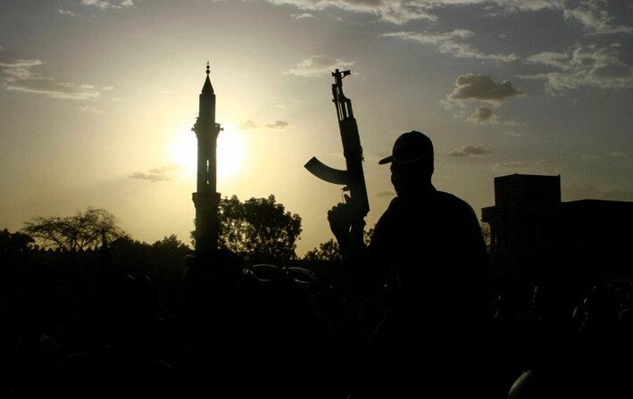 Un combatiente leal al jefe del ejército de Sudán, Abdel Fattah al-Burhan, sostiene un arma frente al minarete de una mezquita durante una ceremonia de graduación en el estado de Gedaref, en el sureste de Sudán, el 27 de mayo de 2024. (AFP vía Getty Images)