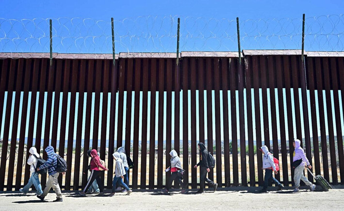 Inmigrantes ilegales caminan por el lado estadounidense del muro fronterizo en Jacumba Hot Springs, California, tras cruzar desde México, el 5 de junio de 2024. (Frederic J. Brown/AFP vía Getty Images)