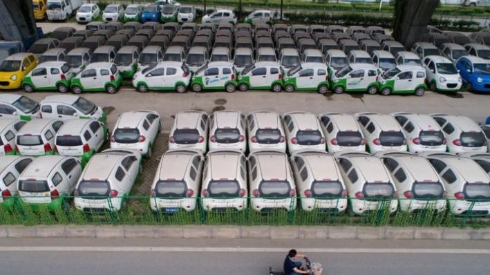 Un automovilista pasa por delante de nuevos vehículos eléctricos estacionados bajo un viaducto en Wuhan, provincia de Hubei, China, el 22 de mayo de 2017. (STR/AFP vía Getty Images)