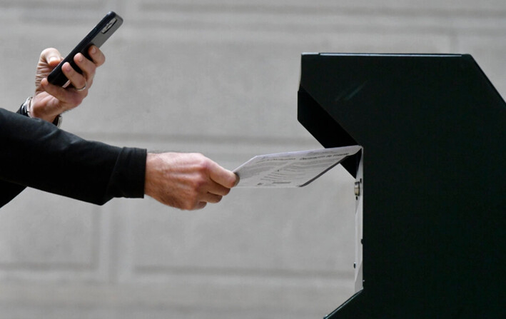 Un hombre se fotografía depositando su papeleta en una urna oficial mientras una larga fila de votantes hace cola fuera del Ayuntamiento de Filadelfia, en el centro de votación satélite en Filadelfia, Pensilvania, el 27 de octubre de 2020. (Mark Makela/Getty Images)