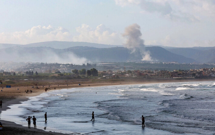 La gente camina en una playa mientras el humo se eleva al fondo en el lado libanés de la frontera con Israel, desde Tiro, en el sur del Líbano, el 22 de septiembre de 2024. (Aziz Taher/Reuters)