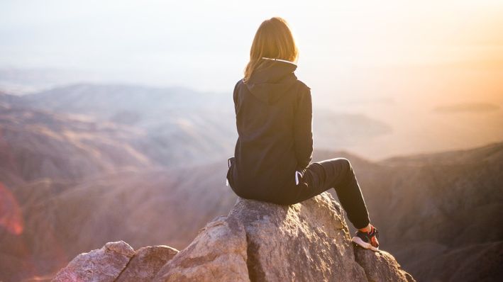 Imagen ilustrativa de una mujer joven sentada en la punta de una montaña. (StockSnap/Pixabay)