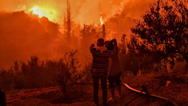 Una pareja observa un incendio forestal que arrasa el pueblo de Ano Loutro, al sur de Atenas, el 30 de septiembre de 2024. Al menos dos personas fueron encontradas muertas y siete pueblos fueron evacuados debido al fuego. (Valerie Gache / AFP vía Getty Images)