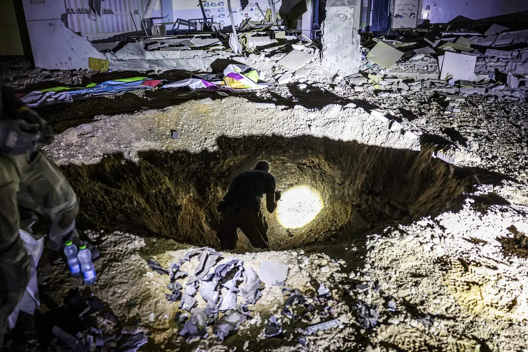 Miembros del Mando del Frente Interior de Israel y fuerzas policiales inspeccionan un cráter dejado por la explosión de un proyectil en un edificio escolar gravemente dañado en la ciudad de Gedera, en el sur de Israel, el 1 de octubre de 202, después de que Irán disparara entre 150 y 200 misiles en un ataque contra Israel. (MENAHEM KAHANA/AFP vía Getty Images)