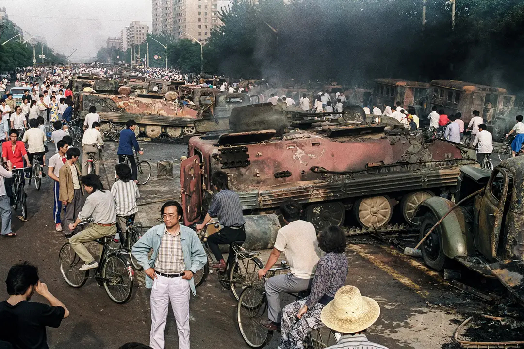 Habitantes de Beijing inspeccionan el interior de uno de los más de 20 vehículos blindados de transporte de tropas quemados por los manifestantes para impedir el paso de las tropas a la plaza de Tiananmen el 04 de junio de 1989. (MANUEL CENETA/AFP vía Getty Images)