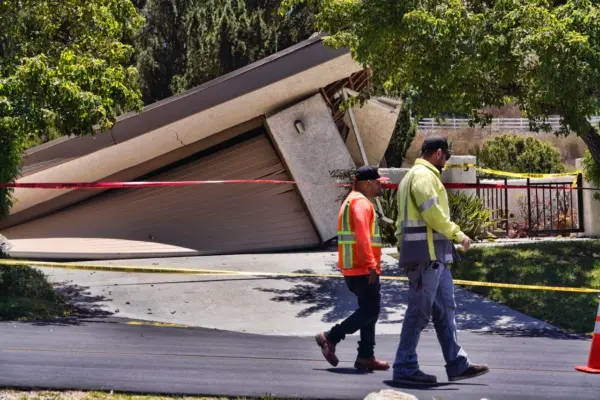 Empleados municipales pasan junto a una casa dañada que se tambalea sobre un barranco en Rolling Hills Estates, en la península de Palos Verdes, en el condado de Los Ángeles, el 10 de julio de 2023. (Richard Vogel/AP Photo)