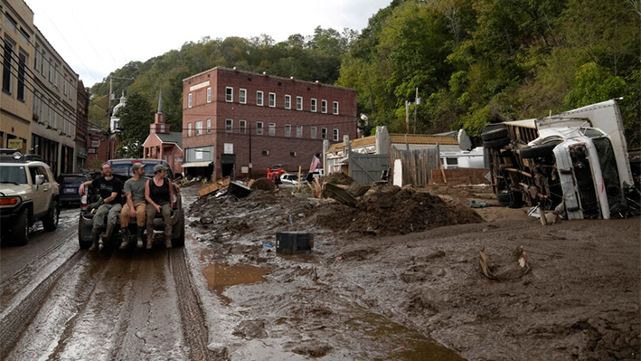 Varias personas viajan en la parte trasera de una camioneta en una calle cubierta de barro tras el paso del huracán Helene, en Marshall, Carolina del Norte, el 1 de octubre de 2024. (AP Photo/Jeff Roberson)