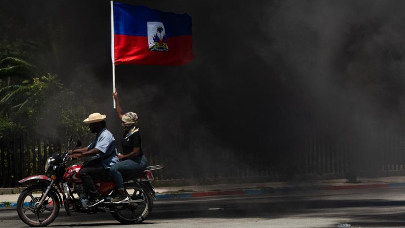 Fotografía de archivo del 7 de agosto de 2023 de una persona que ondea una bandera haitiana en medio del humo, durante una marcha para exigir seguridad contra las pandillas, en Puerto Príncipe (Haití). EFE/ Johnson Sabin
