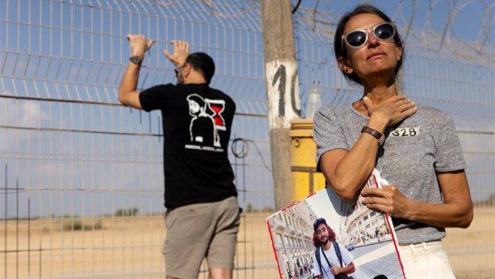 Rachel Goldberg, la madre del rehén Hersh Goldberg-Polin que fue secuestrado el 7 de octubre en un ataque mortal de Hamás, sostiene su foto mientras los familiares de los rehenes utilizan altavoces gigantes para llamar a sus seres queridos cautivos cerca de la frontera con la Franja de Gaza en Nirim, Israel, el 29 de agosto de 2024. (Amir Levy/Getty Images)