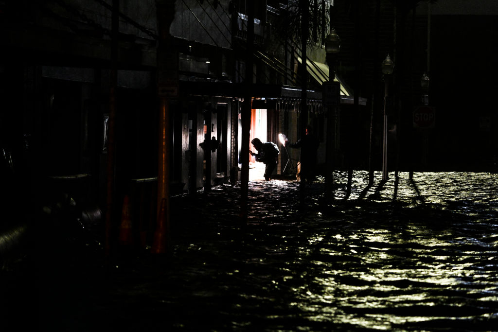 La gente usa sus teléfonos para tomar fotografías y encender luces mientras caminan por calles inundadas después de que el huracán Milton tocara tierra en Fort Myers, Florida, el 9 de octubre de 2024. (Chandan Khanna/AFP vía Getty Images)