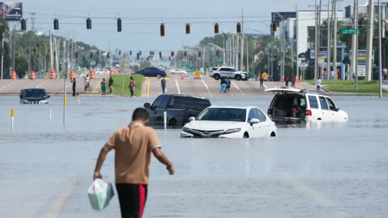 Un hombre camina junto a vehículos en las calles inundadas por el huracán Milton en la sección sureste de Seminole Heights de Tampa, Florida, el 10 de octubre de 2024. (Bryan R. Smith/AFP vía Getty Images)