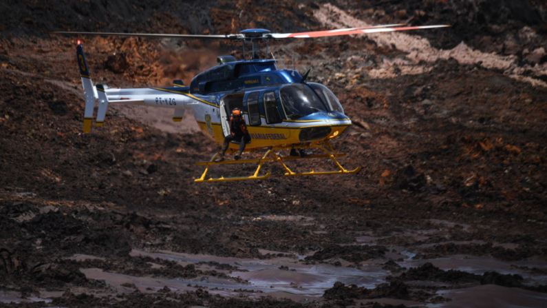 Un helicóptero sobrevuela la zona en la que trabajan rescatistas y bomberos en la búsqueda de víctimas de un colapso de una represa en una mina de mineral de hierro, cerca de la localidad de Brumadinho, estado de Minas Gerais, sureste de Brasil, el 28 de enero de 2019. (Mauro Pimentel/AFP vía Getty Images)