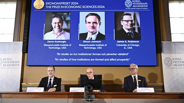 El secretario permanente de la Academia de las Ciencias, Hans Ellegren, (C), Jakob Svensson, (I), y Jan Teorell, de la asamblea Nobel, anuncian los ganadores del premio Nobel de Economía, Daron Acemoglu, Simon Johnson, y James A Robinson, vistos en pantalla, durante un encuentro con la prensa en la Real Academia Sueca de las Ciencias en Estocolmo, Suecia, el 14 de octubre de 2024. (Christine Olsson/Agencia de Noticias TT vía AP)