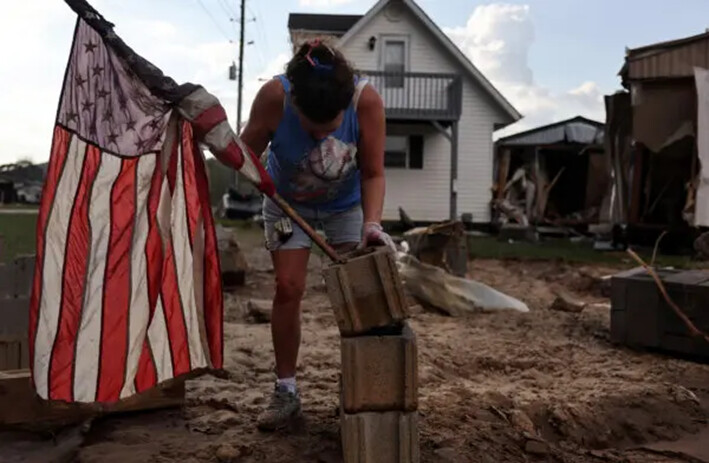 Roxanne Brooks monta una bandera estadounidense en una pila de bloques de hormigón fuera de la casa móvil destruida de su amiga (der.) tras las inundaciones provocadas por el huracán Helene, en Swannanoa, Carolina del Norte, el 6 de octubre de 2024. (Mario Tama/Getty Images)