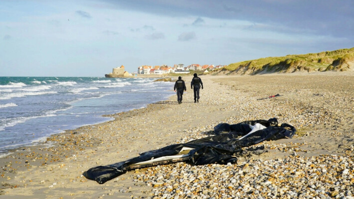 La policía francesa pasa junto a un bote desinflado en la playa de Wimereux, cerca de Calais, Francia, el 18 de noviembre de 2021. (Gareth Fuller/PA).