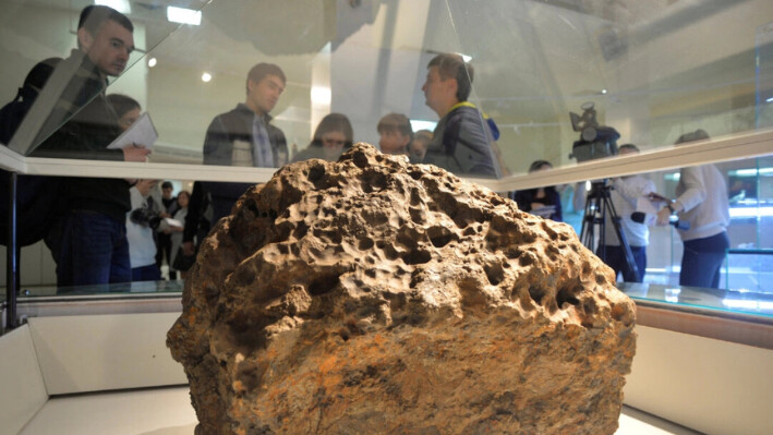 Los reporteros se reúnen alrededor de una pieza de un meteorito, que según las autoridades locales y los científicos fue levantado del fondo del lago Chebarkul, colocado en exhibición en un museo local en Chelyabinsk, el 18 de octubre de 2013. (Andrey Tkachenko/Reuters)